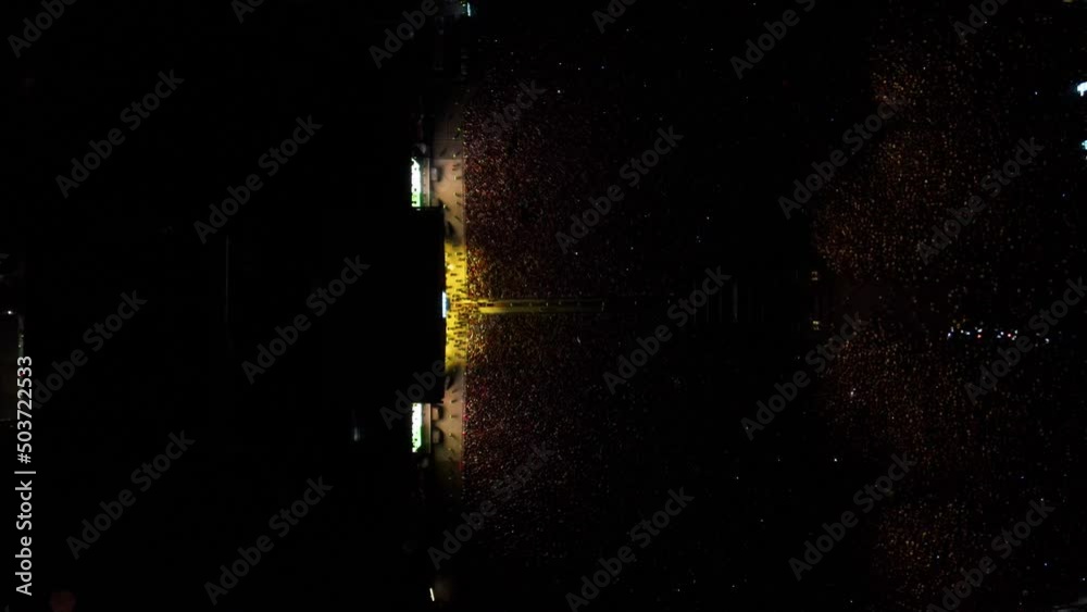 toma cinemática de drone en cenital de Multitud de gente espectadora de un concierto en un festival de música latina con luces amarillas iluminándolos 