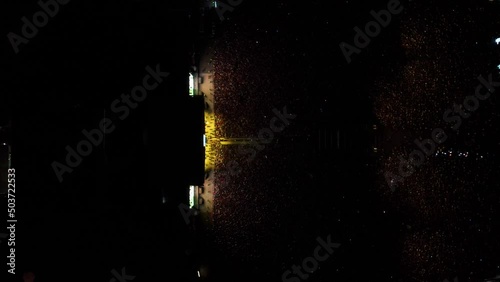 toma cinemática de drone en cenital de Multitud de gente espectadora de un concierto en un festival de música latina con luces amarillas iluminándolos 