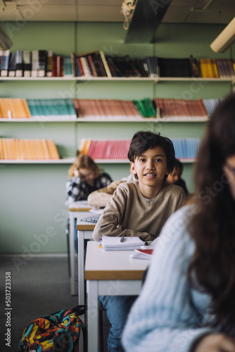 Schoolboy sitting on desk in classroom