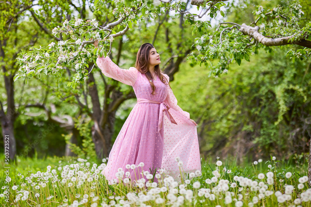 a young woman in a pink dress posing next to a blossoming apple, spring portrait. a young woman in a pink dress posing next to a blossoming apple, spring portrait.
