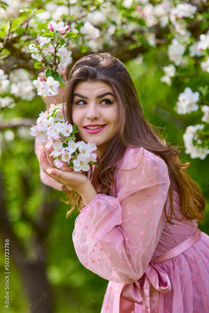 Obraz premium a young woman in a pink dress posing next to a blossoming apple, spring portrait.