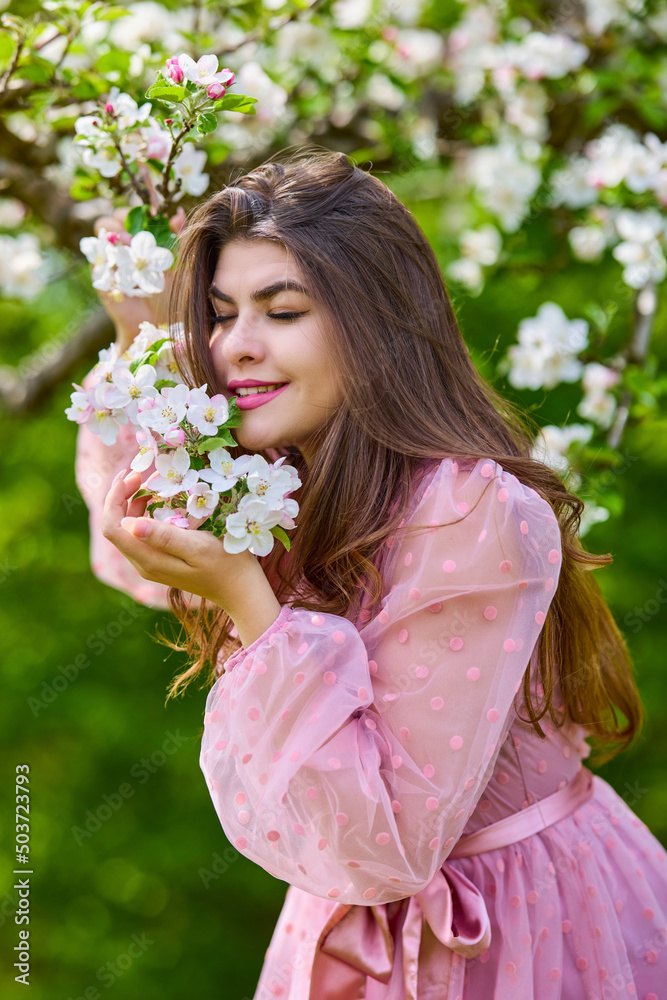 Fototapeta premium a young woman in a pink dress posing next to a blossoming apple, spring portrait.