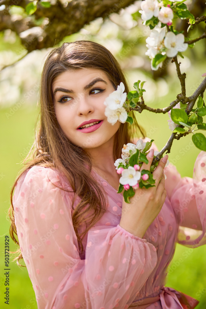 Fototapeta premium a young woman in a pink dress posing next to a blossoming apple, spring portrait.