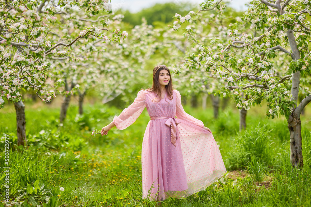 a young woman in a pink dress posing next to a blossoming apple, spring portrait. a young woman in a pink dress posing next to a blossoming apple, spring portrait.