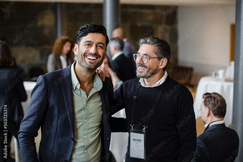 Portrait of happy businessman with male delegate at seminar in convention center Portrait of happy businessman with male delegate at seminar in convention center