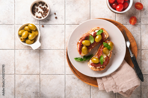 Bruschetta with sun dried tomatoes. Toast or sandwich with ricotta, sun dried tomatoes and Provence herbs with basil servered on a plate on a grey old cracked tile table. Top view banner menu recipe. photo