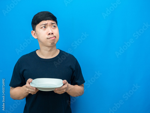 Asian man gesture hungry holding dish and looking at copy space thiking about dinner