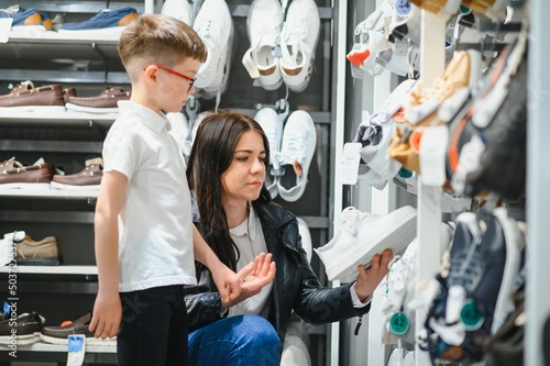 woman with child choosing and trying on new boots in shopping mall