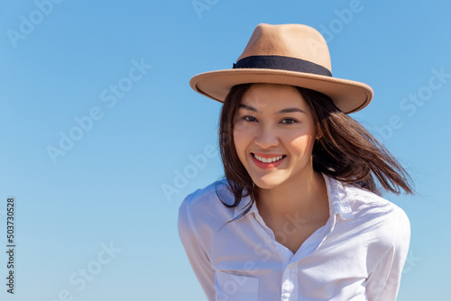 Portrait happy attractive young Asian woman wear hat looking at camera in the bright sunny day summer blue sky. Millennial lady with smiley face on her vacation holiday trip in tropical location