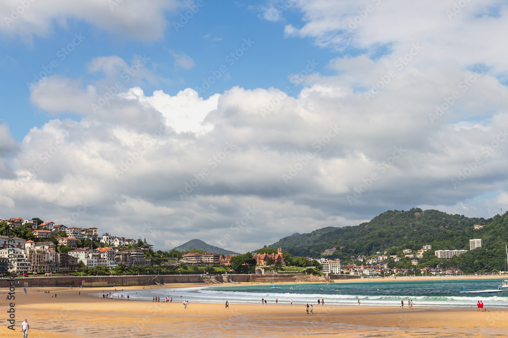 Naklejka premium Wide sandy beach with people walking on a sunny day on the ocean coast in the Spanish city of San Sebastian