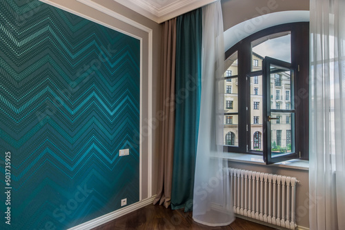 The original design of the room with turquoise silk-screen printing on the wall and a beautifully draped arched window.