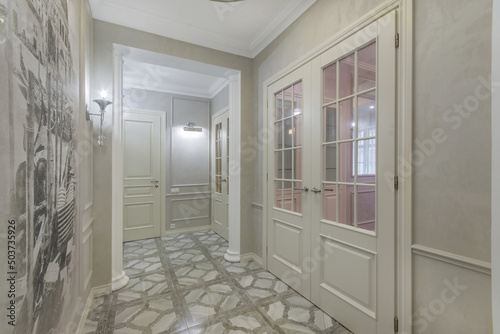 A beautiful bright corridor with large interior doors, a mosaic ceiling lamp and brown ceramic floor tiles.Neoclassical interior design