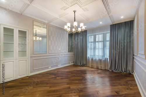 A spacious living room without furniture with original decorated walls and ceiling. Brown parquet.