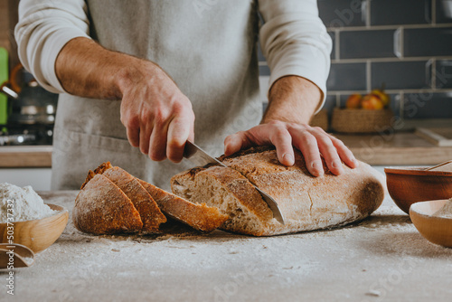 Young man in apron cutting homemade bread