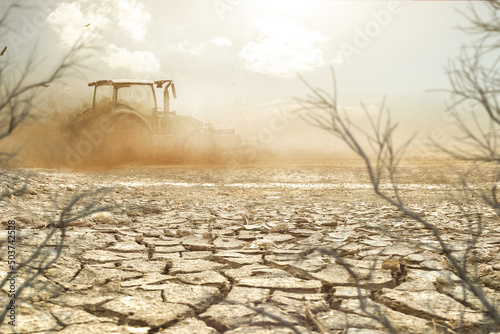 Valokuvatapetti Traktor pflügt ein Feld bei Trockenheit