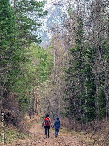 Mom and son are going hiking on a forest road uphill. © vadim