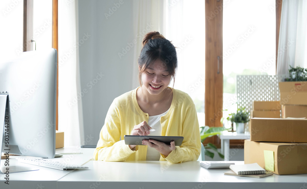 Portrait business Asian woman smile and use tablet checking information on parcel shipping box before send to customer. Entrepreneur small business working at home. SME business online marketing. Portrait business Asian woman smile and use tablet checking information on parcel shipping box before send to customer. Entrepreneur small business working at home. SME business online marketing.