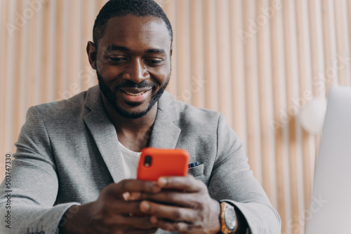 Cheerful young afro american man chatting online on smartphone looking on phone screen with smile