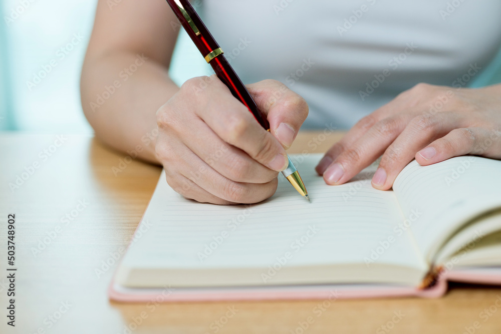 Hands writing in notepad on wooden table Hands writing in notepad on wooden table