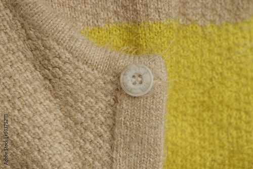 one white plastic button on gray yellow wool sweater fabric