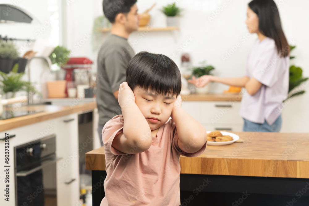 Little asian sad boy, unhappy while parents fighting, kid son not listen to shouting noise while mom and dad arguing, quarrel behind. Family suffering, stressed. Violence and divorce couple concept. Little asian sad boy, unhappy while parents fighting, kid son not listen to shouting noise while mom and dad arguing, quarrel behind. Family suffering, stressed. Violence and divorce couple concept.
