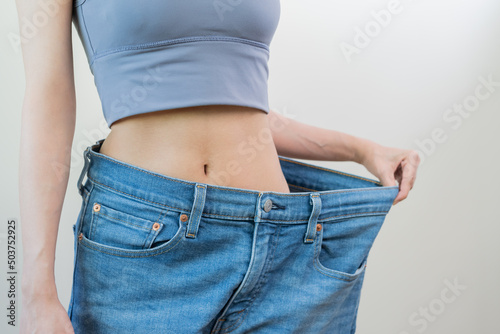 Shape slender, thin waist, attractive slim asian young woman, hand show shape her weight loss, wearing in big, large or oversize jeans, excess lose by diet and exercise. People body fit healthy. © KMPZZZ
