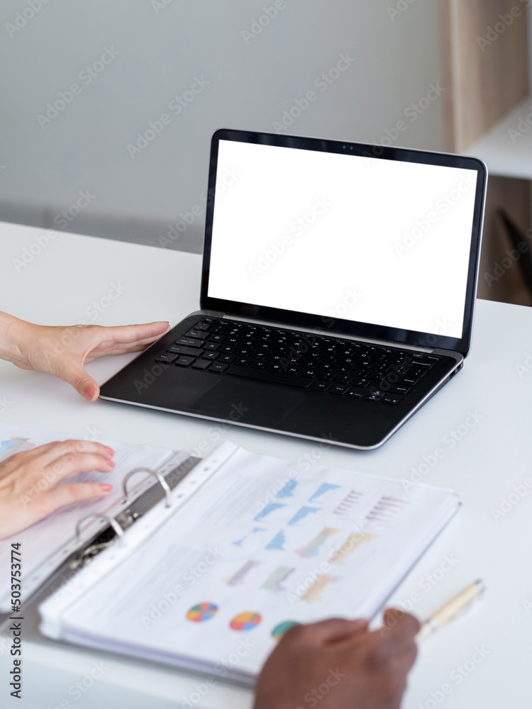 Business work. Office colleagues. Computer mockup. Unrecognizable man and woman looking laptop blank screen with report on desk in light room interior. Business work. Office colleagues. Computer mockup. Unrecognizable man and woman looking laptop blank screen with report on desk in light room interior.