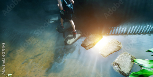 Tableau sur toile Male hiker with backpack crossing a river on stones