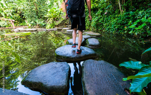 фотографія Male hiker with backpack crossing a river on stones