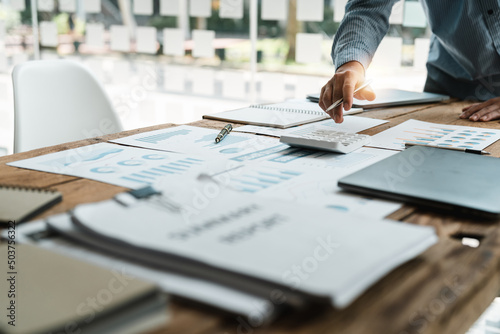 Close up of businessman or accountant hand holding pen working on calculator to calculate business data, accountancy document and laptop computer at office, business concept