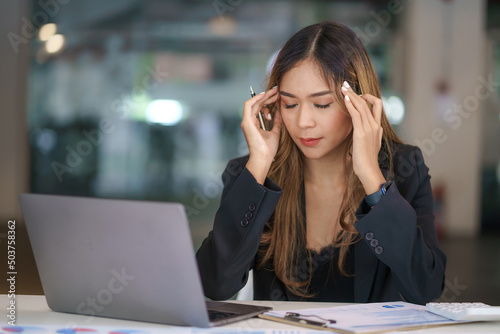 Overworked and stressed young Asian woman sitting at workplace in office.