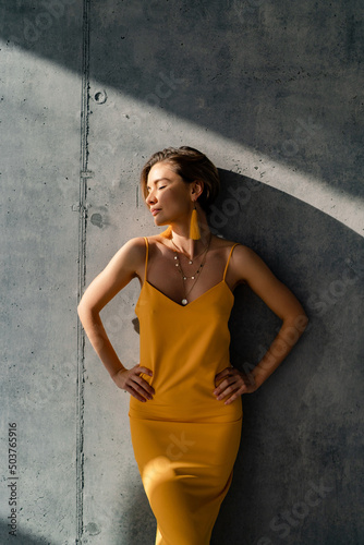 attractive woman in yellow summer dress in interior room concrete wall background