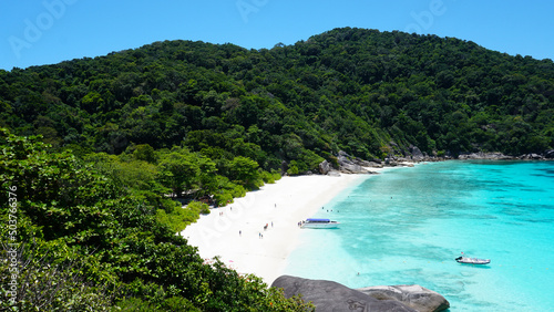 Turquoise water in the bay. View of the island and the sea. High cliffs covered with green trees. The gradient of water from blue to blue. There are speedboats, people swim in places. Similan Islands
