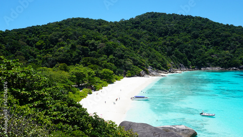 Fototapeta Naklejka Na Ścianę i Meble -  Turquoise water in the bay. View of the island and the sea. High cliffs covered with green trees. The gradient of water from blue to blue. There are speedboats, people swim in places. Similan Islands