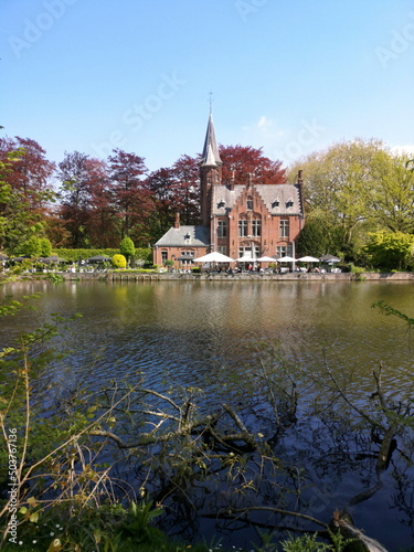 Blick vom Ufer des Minnewater auf das gegenüberliegende Kasteel Minnewater vor blauem Himmel im Sonnenschein in der Altstadt von Brügge in Westflandern in Belgien photo