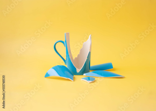 A broken blue cup with shards around on a yellow background