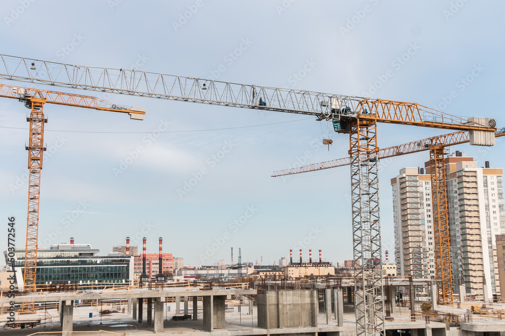 Construction cranes at a construction site in the city against the blue sky. Construction of a new building. The concept of building a new area. Construction cranes at a construction site in the city against the blue sky. Construction of a new building. The concept of building a new area.