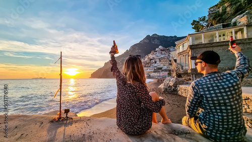 Tourist couple having drink and watching sunset on Marina Grande Beach. Golden hour in hillside village Positano at Amalfi Coast, Italy, Campania, Europe. Vacation at Tyrrhenian, Mediterranean Sea photo