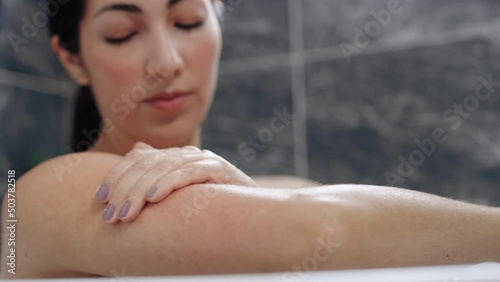 Beautiful woman rubs exfoliating body scrub along her arm during a bath in slow motion