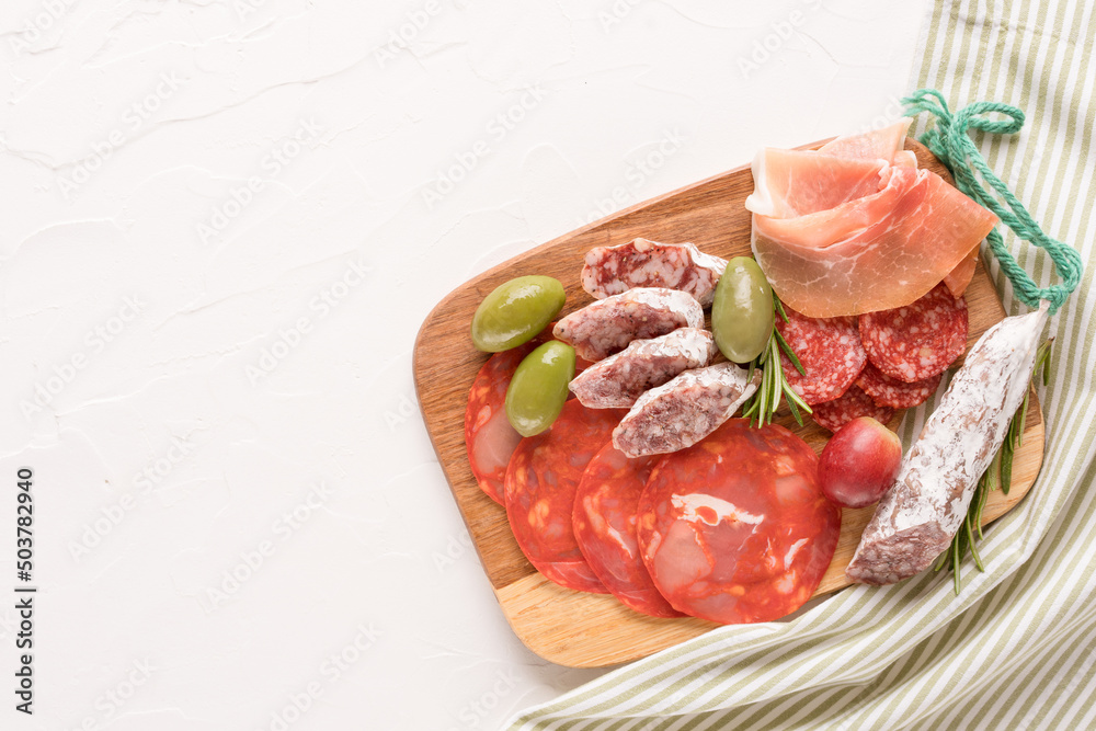 Variety of meat snacks, charcuterie plate with different types of sausages - salami, bresaola, proscuitto served with olives, rosematy and fresh grape. Wooden cutting board with italian antipasti