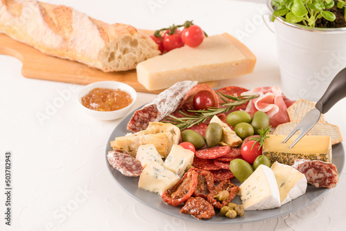 Antipasti plate with variety of cheeses, sausages served with sun dried tomatoes, olives, jams and herbs on white table - parmesan, dorblu, prosciutto, salami. Cheese and meat snacks platter