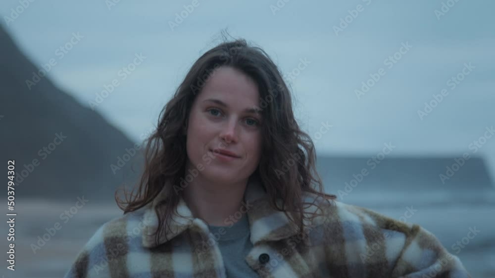 Closeup portrait of pretty happy carefree teenage female with brunette curly windy hair wearing casual cosy plaid shirt, smiling, dreaming, looking at camera at grey seashore cold ocean water, waves Closeup portrait of pretty happy carefree teenage female with brunette curly windy hair wearing casual cosy plaid shirt, smiling, dreaming, looking at camera at grey seashore cold ocean water, waves