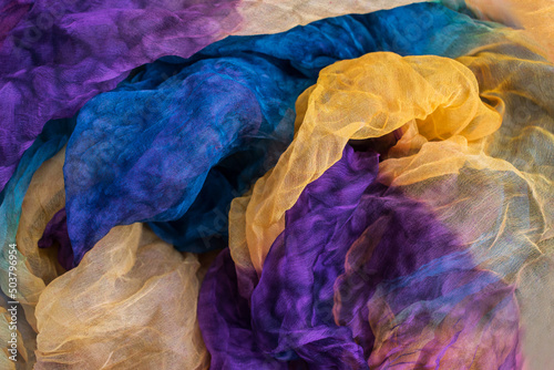 A photo of fabric dyed yellow, blue, purple colors and laid out in an abstract form for use as a background.