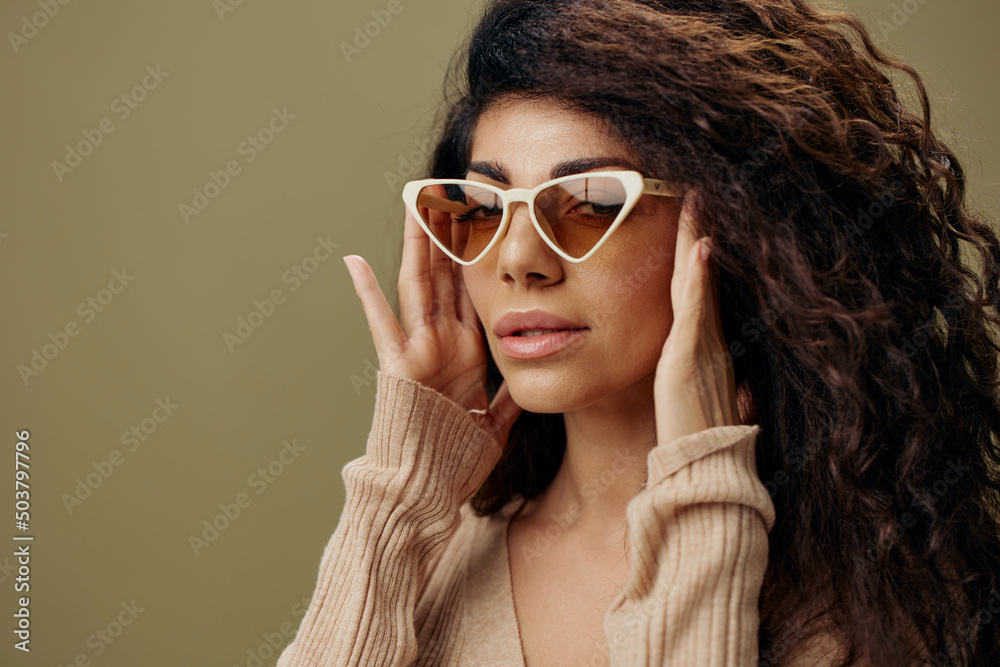 Naklejka premium STYLISH EYEWEAR CONCEPT. Happy adorable tanned curly Latin female in casual things wear trendy sunglasses posing isolated over olive green background. Copy space Mockup Banner. Fashion closeup offer