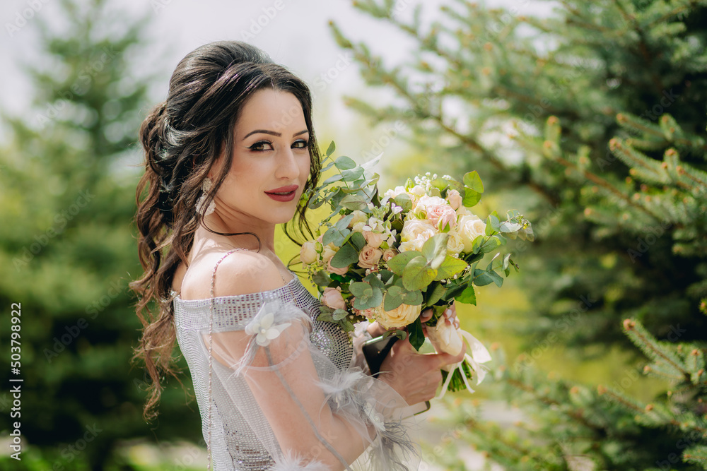 Natural dreamy portrait of cute, smiling bridesmaid standing next to the pine tree and posing for camera
