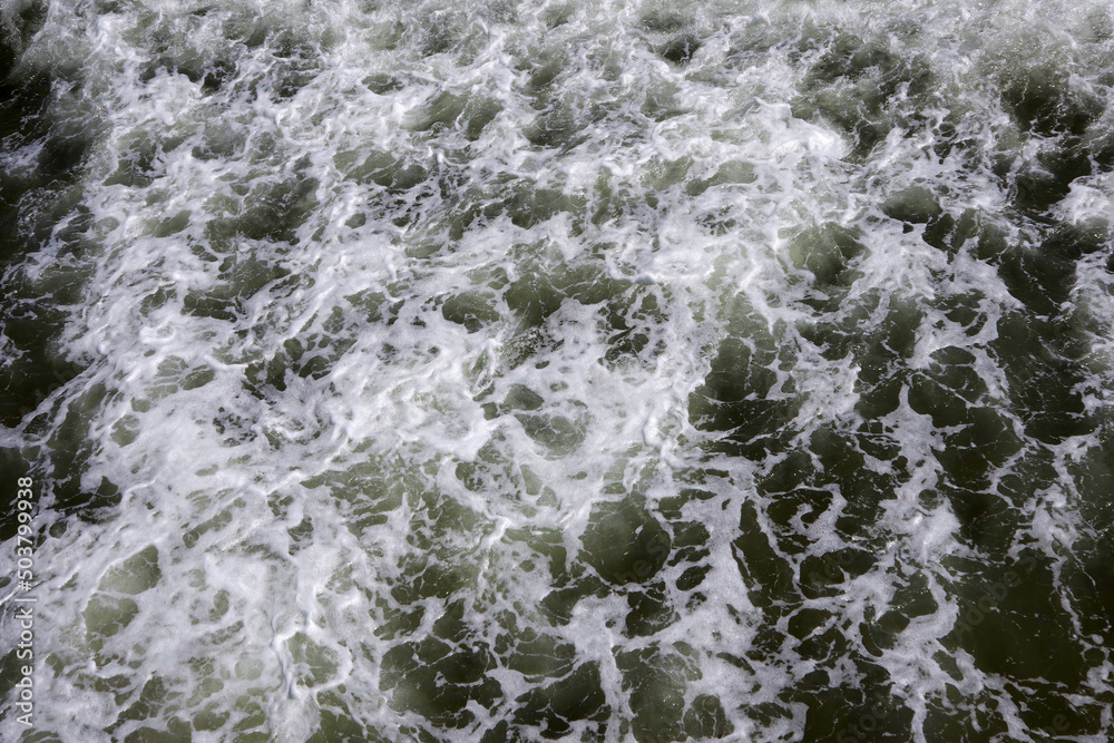 Bubbling and white foaming dark ocean water surface