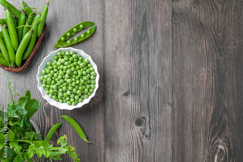 Fotobehang Fresh organic raw green peas in a bowl with peas plants leaves on dark wooden table background