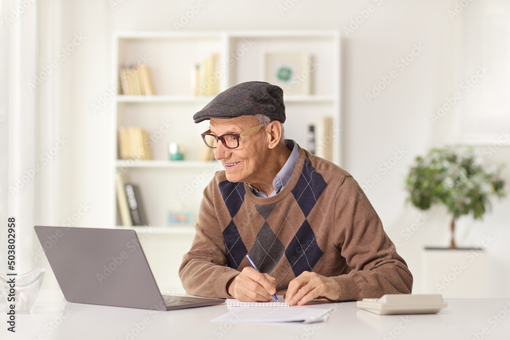Elderly man writing on a paper and looking at a laptop computer Elderly man writing on a paper and looking at a laptop computer