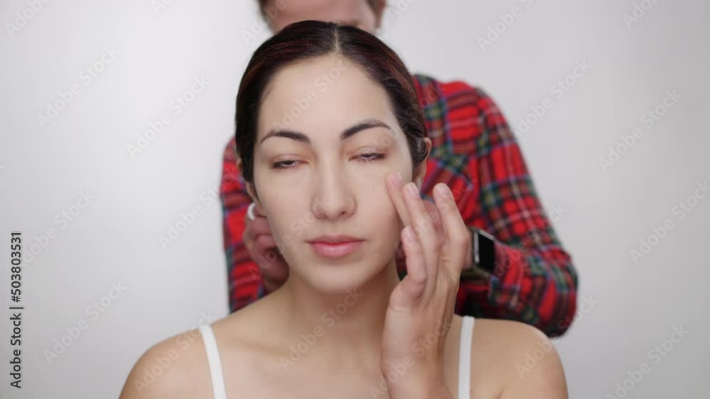 Pretty model blends, smooths makeup with fingertips as hair stylist fixes hair Pretty model blends, smooths makeup with fingertips as hair stylist fixes hair