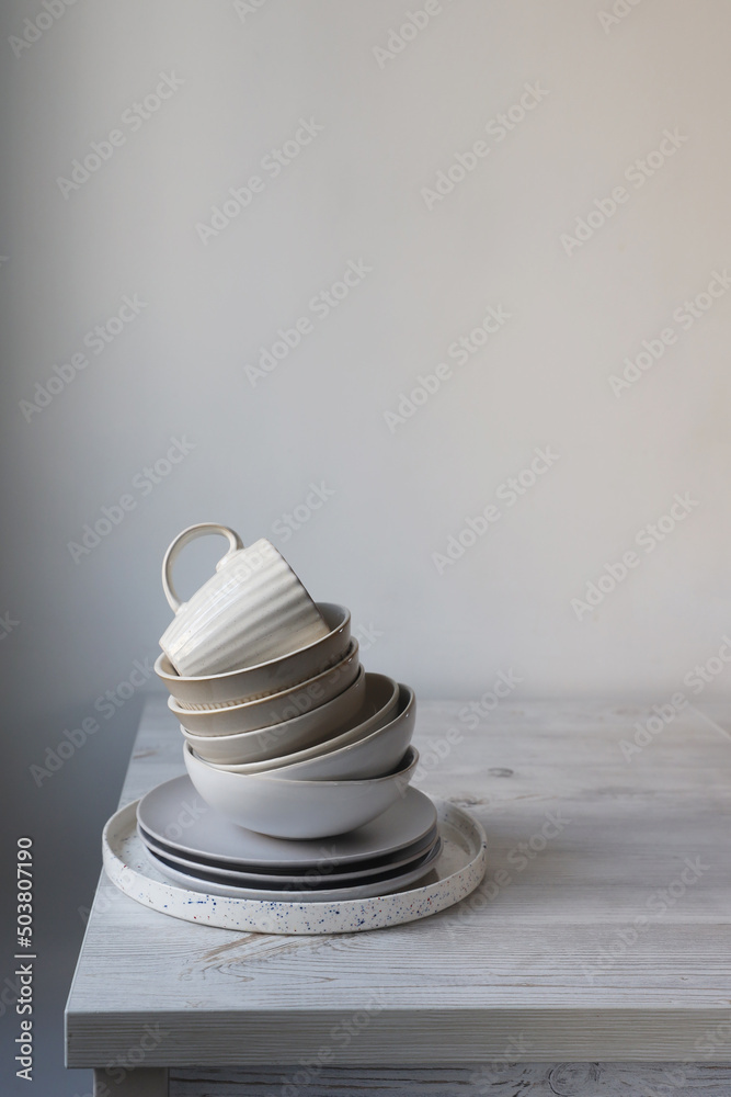 A pyramid of white bowls, plates and cups of different sizes and colors on a beige table in the kitchen. Scandinavian style. Place for your text. Copy space A pyramid of white bowls, plates and cups of different sizes and colors on a beige table in the kitchen. Scandinavian style. Place for your text. Copy space